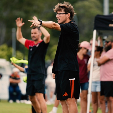 Person in black athletic wear with red stripes on shorts, pointing towards the camera on a sports field.